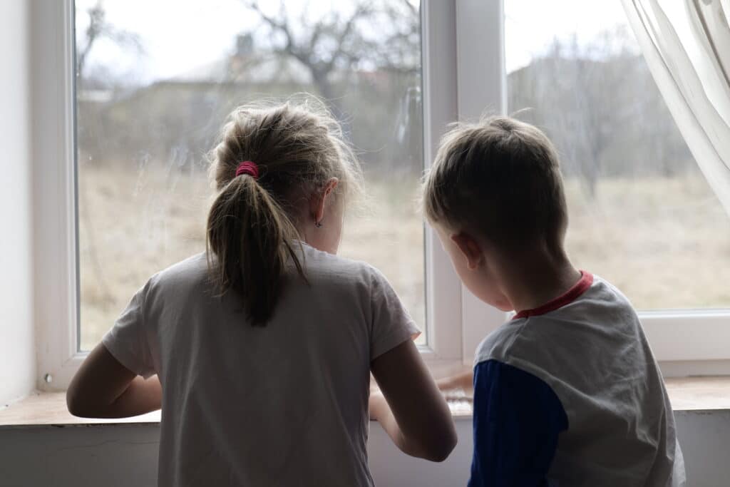 2 barn leker med noe i en vindueskarm, med ryggen til kamera.