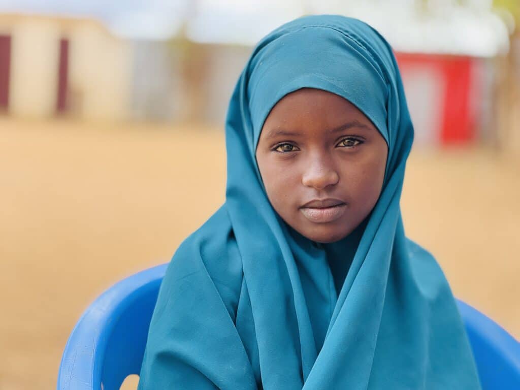 En jente fra Somalia ikledd blå hijab ser inn i kamera