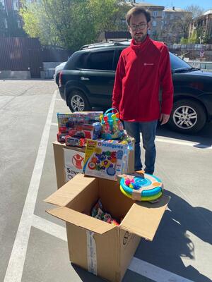 En Redd Barna-ansatt står på en parkeringsplass med 2 pappesker fulle av leker