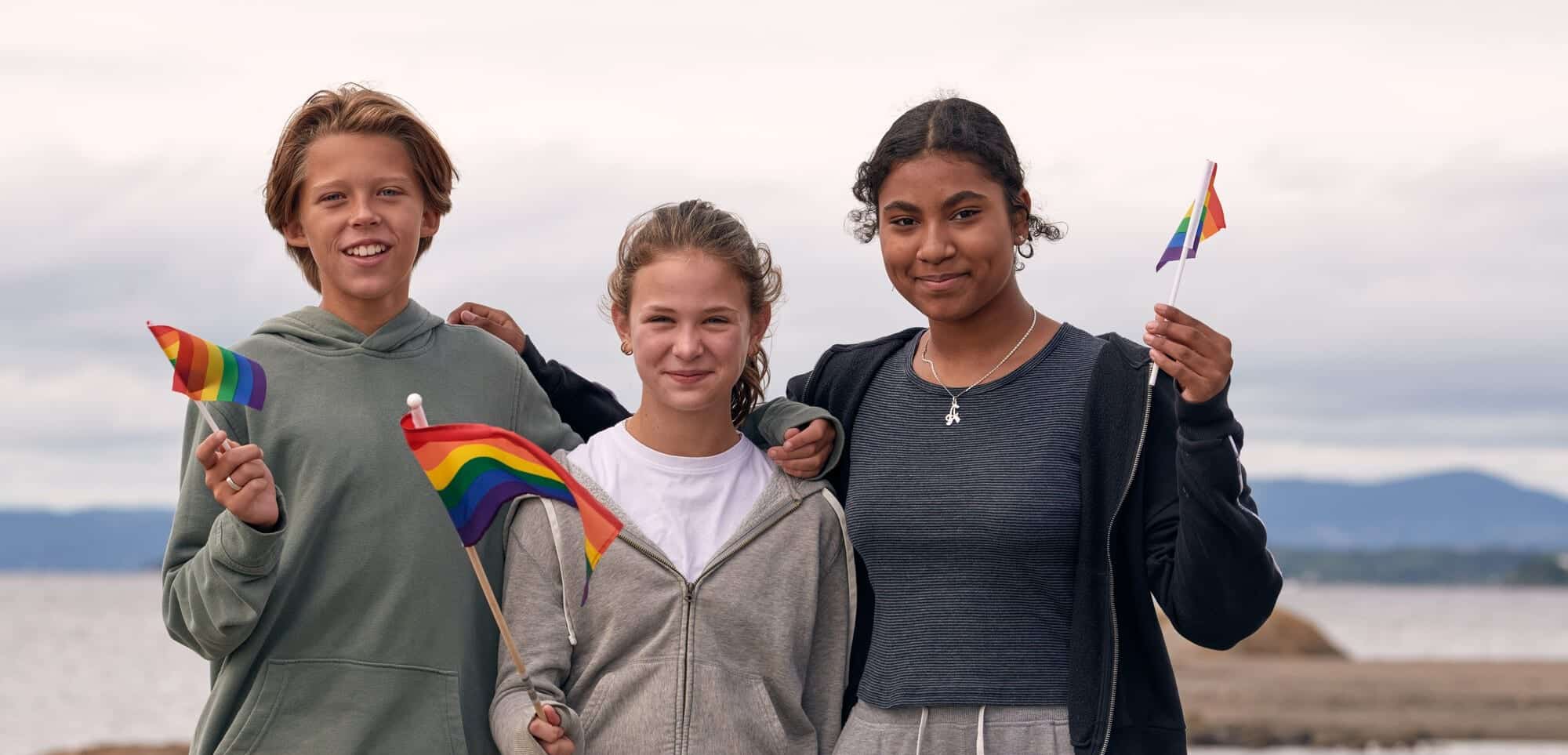 Tre ungdommer har prideflagg og ser inn i kameraet