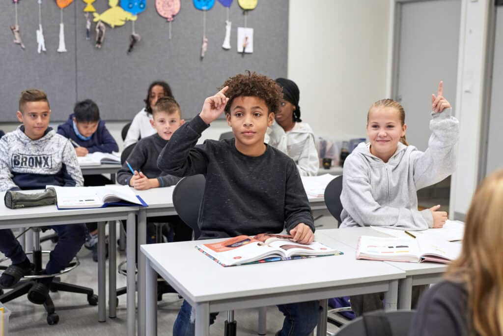 To elever rekker opp hånden i et klasserom
