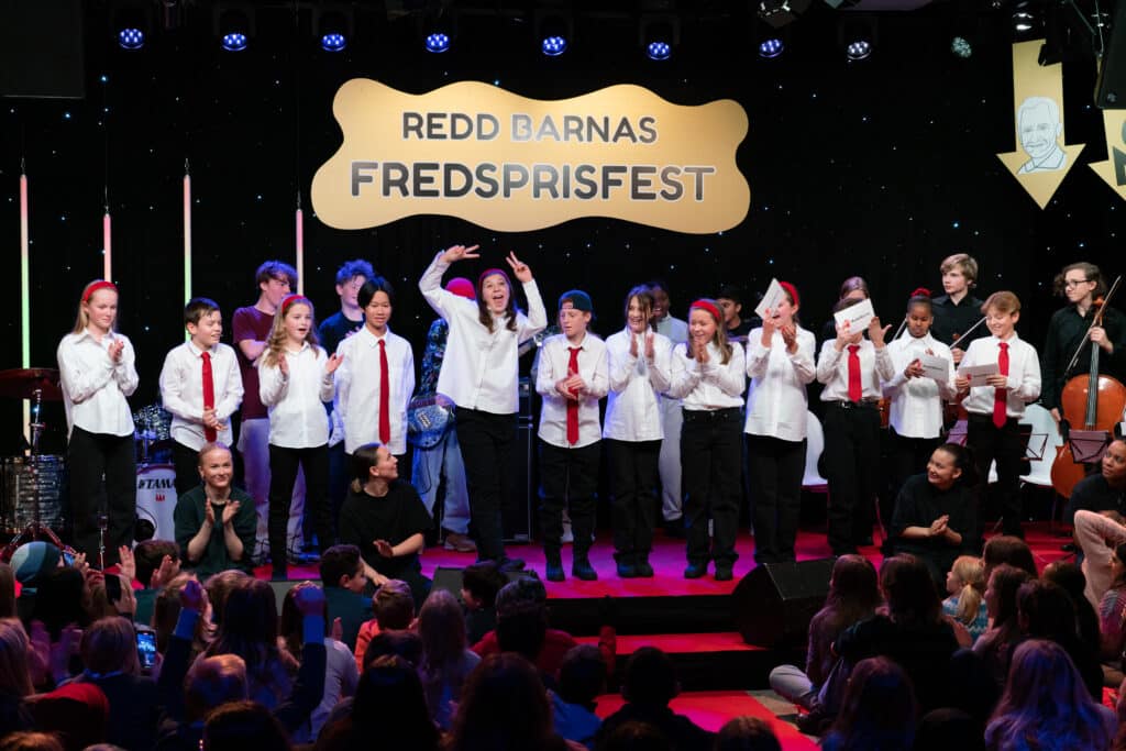 Bilde fra Redd Barnas fredsprisfest 2023. Vi ser barn i salen og tolv elever i festkomiteen på scenen.