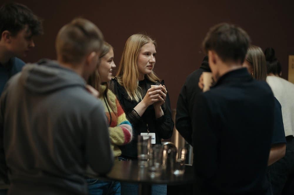 En gjeng mennesker står flokket sammen rundt et lite bord og diskuterer