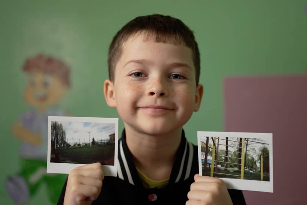 Foto av ukrainsk skolegutt som ser inn i kamera, han holder opp to fotografier,
