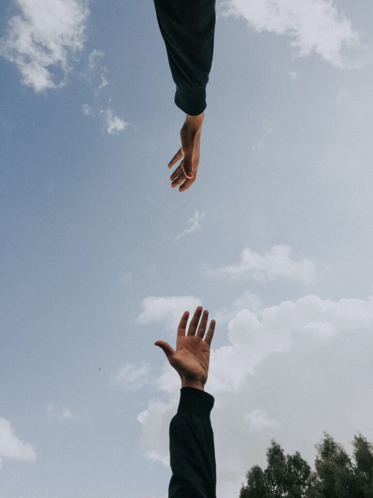 To hender til ungdommer som strekker seg mot hverandre ses nedenfra med blå himmel over.