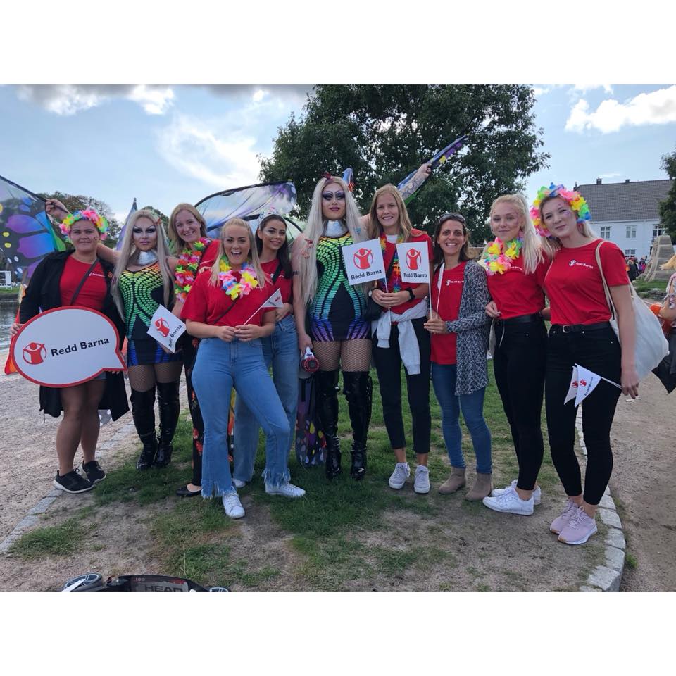 Frivillige fra Redd Barna Kristiansand i røde t-skjorter, fargerik sminke i fjeset og blomsterkranser rundt halsen under Skeive Sørlandsdager