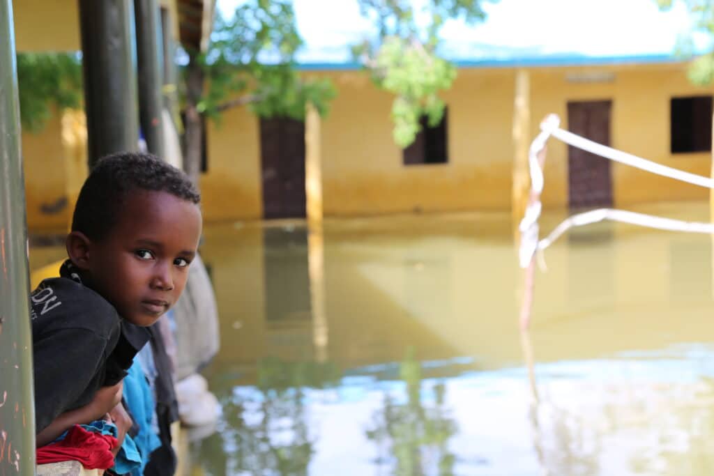 En gutt kikker ut av huset sitt i Somalia, på den oversvømte gaten utenfor - et resultat av verdens klimakrise.