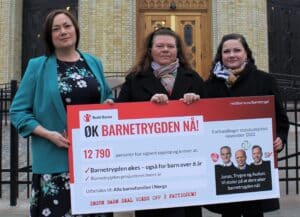 Foto av medlemmer av familie- og oppvekstkomiteen som mottar barnetrygdsjekk fra Redd Barna