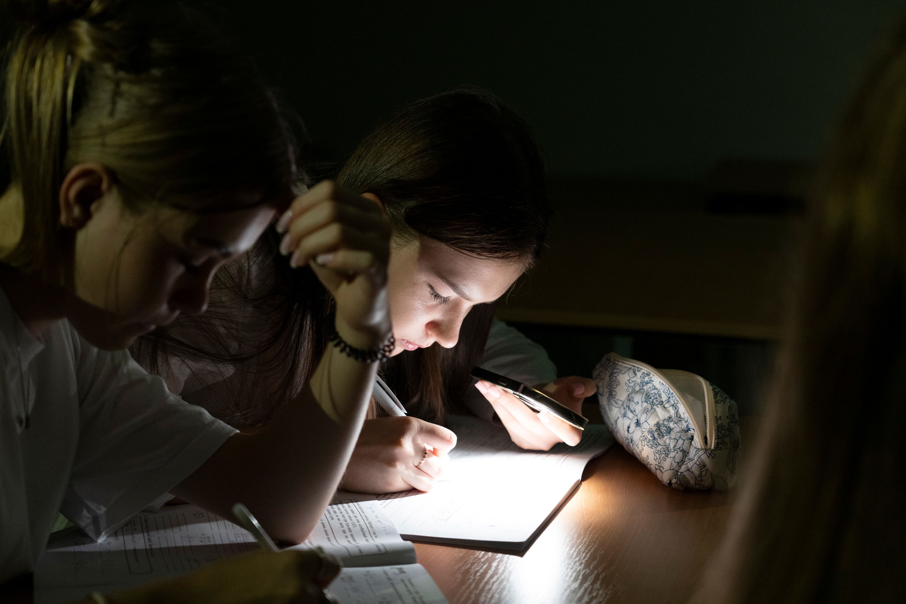 To jenter sitter ved siden av hverandre og lyser ned på skolebøkene sine.
