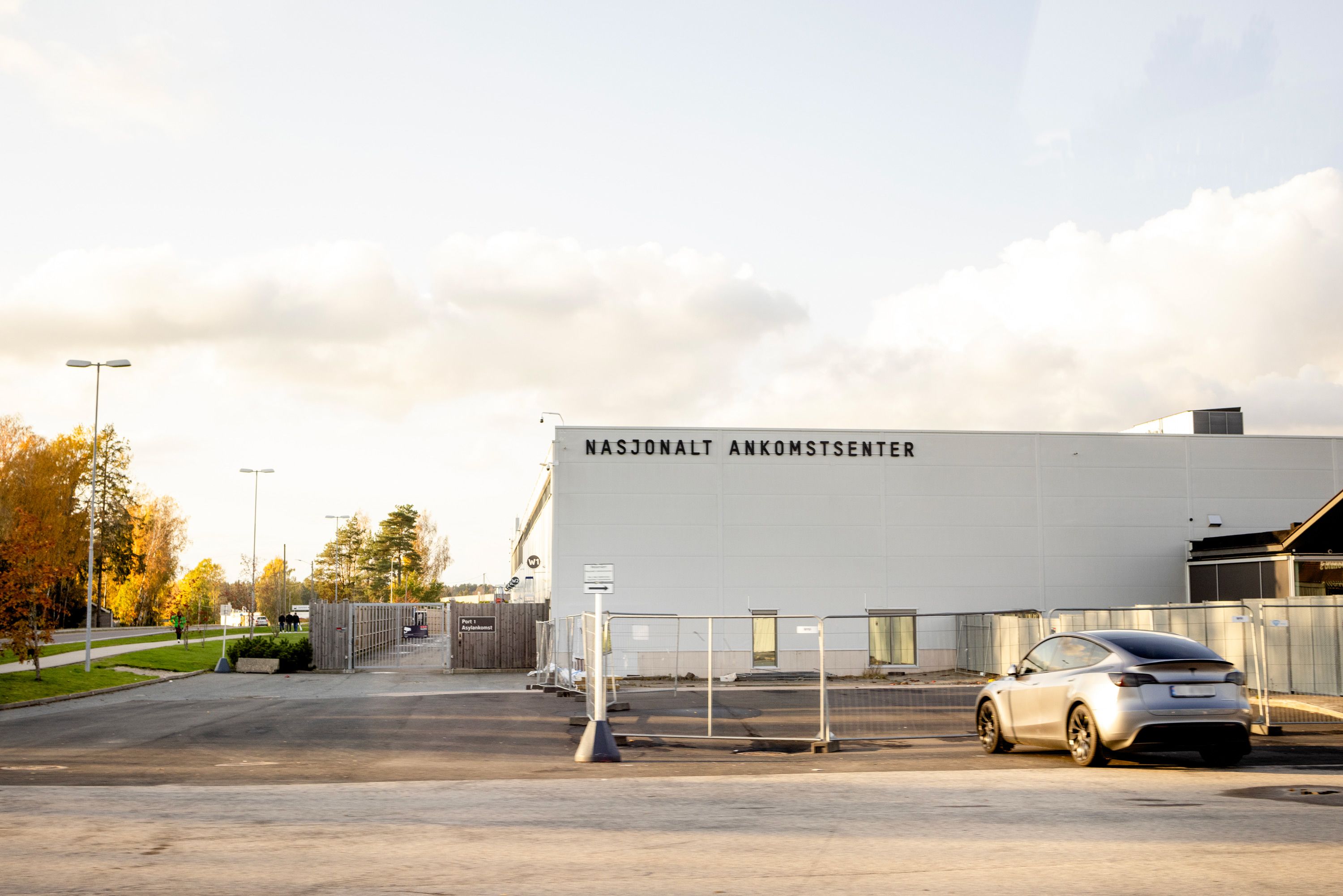 Bilde av en stor grå bygning uten vinduer ved en parkeringsplass. På bygningen er det skrevet “Nasjonalt ankomstsenter” i store bokstaver. 