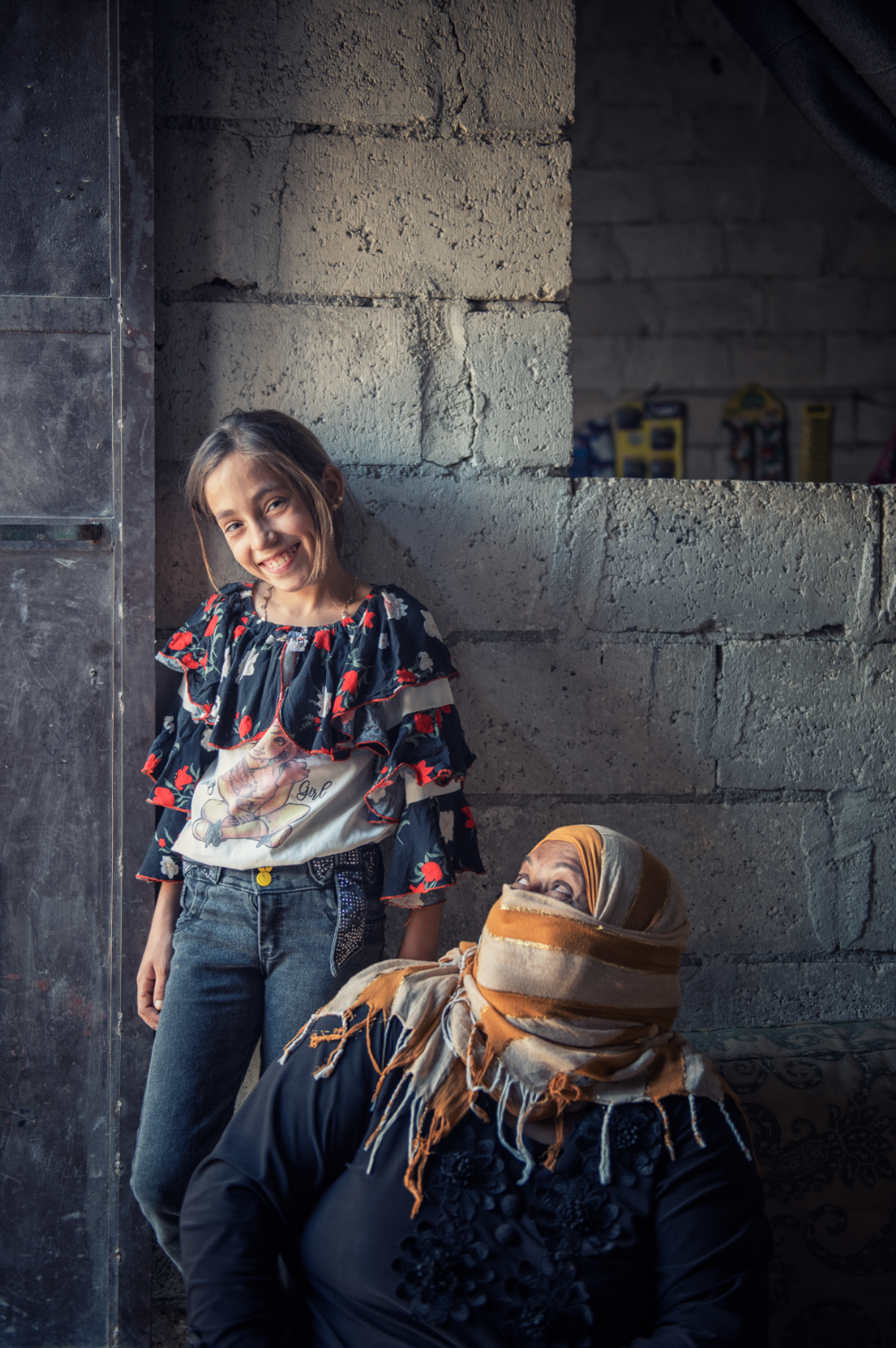 Nadia sitter på gulvet og ser med smilende øyne opp på Aisha (11).