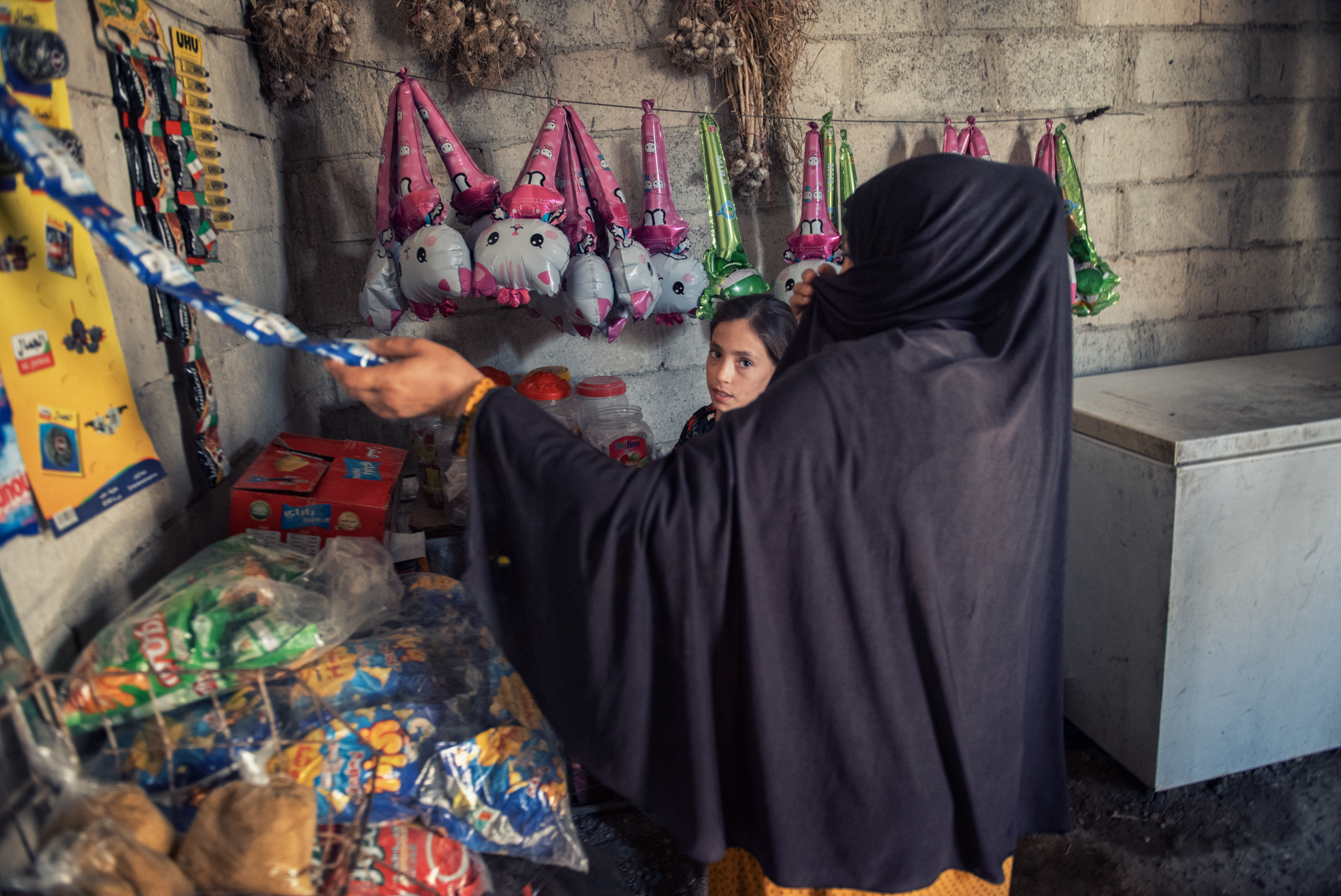 Aisha (11) ser inn i kamera, mens Nadia ser på en remse med produkter som henger på butikkveggen.