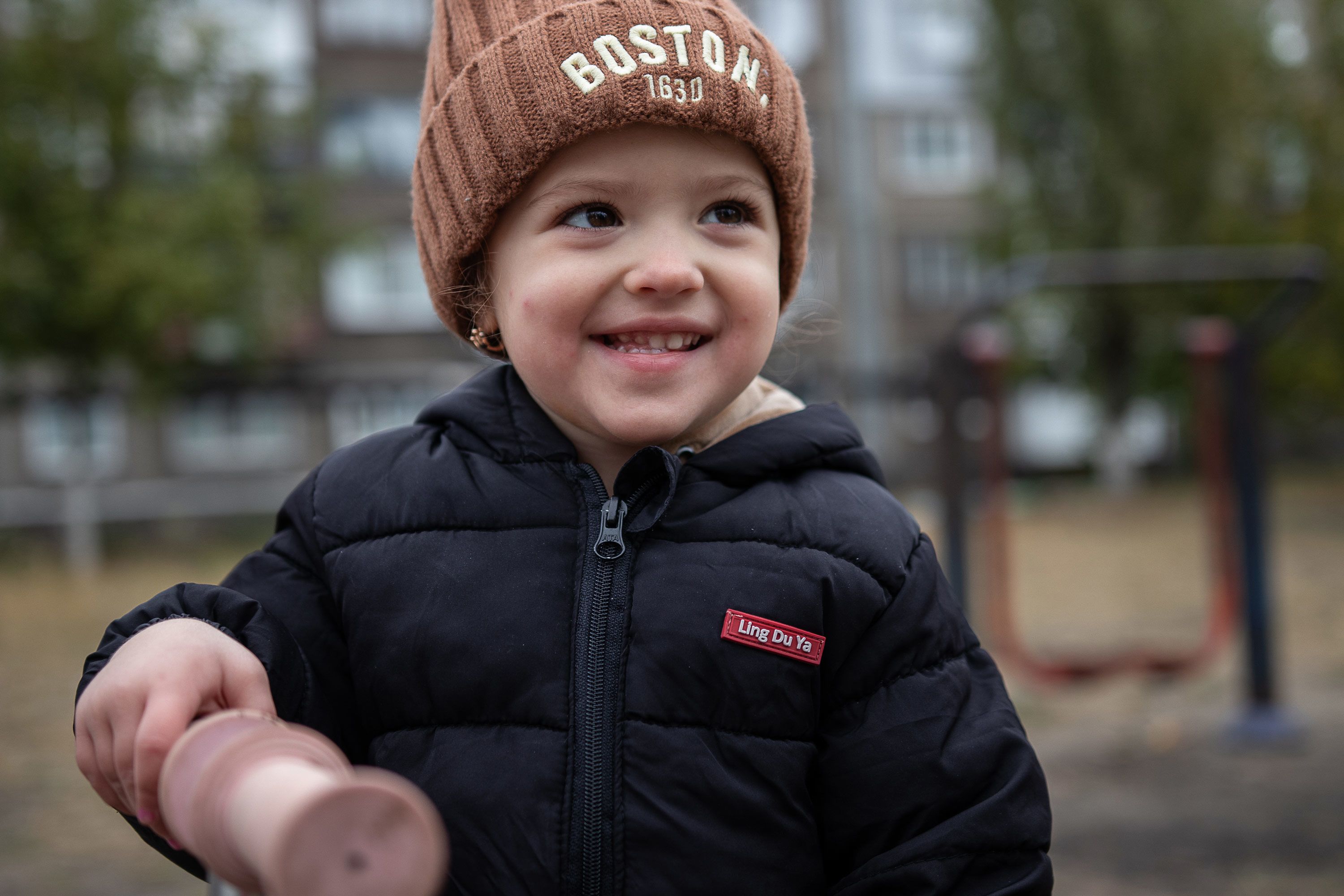 En liten jente med lue og boblejakke står ute og smiler. 