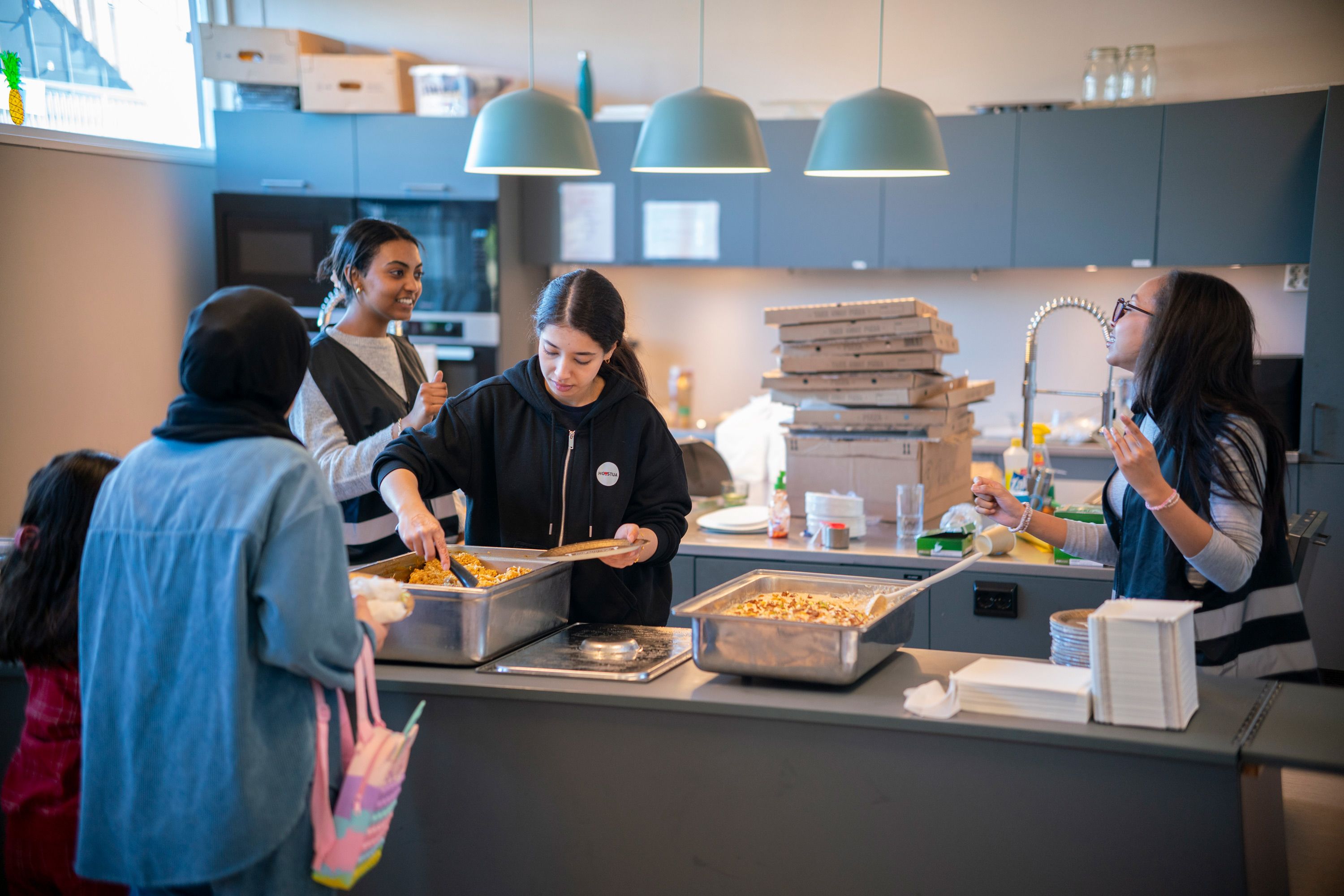 Nour stå bak kjøkkenbenken og serverer mat fra de store beholderne.